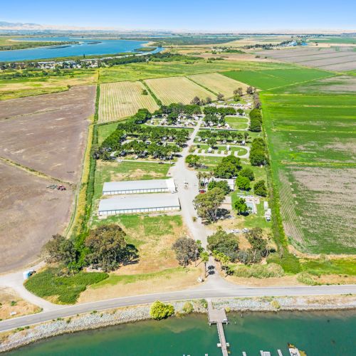 An aerial view of a rural area with fields, trees, buildings, and a body of water. A dock extends into the water.