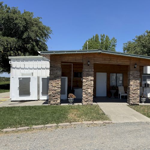 A small building with a stone facade, flat roof, surrounded by grass and trees under a clear blue sky.