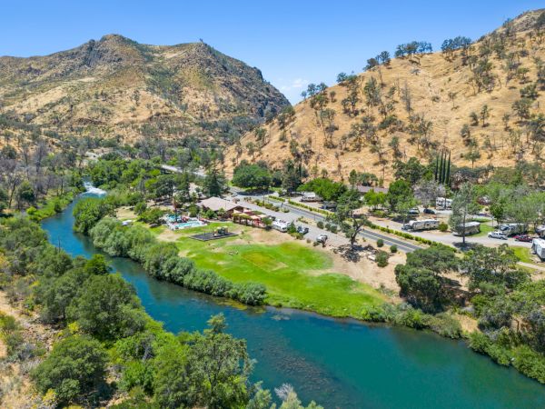 A river flows through a valley with green areas and surrounding hills, and there are buildings near the river's edge.