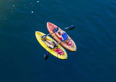 Two people are kayaking on a calm body of water, each in a different colored kayak, gliding closely together.